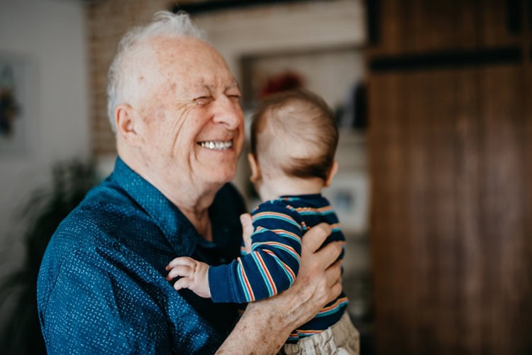 Elderly man hugging a young child, smiling warmly indoors.