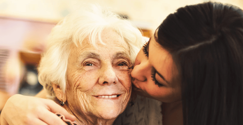 Elderly woman receiving care and affection from a caregiver at home.