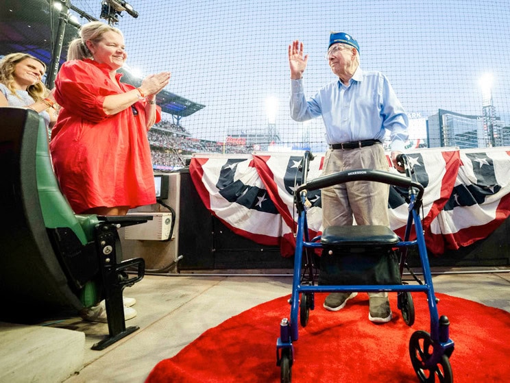 Elderly veteran taking oath at a patriotic event with caregivers and family.